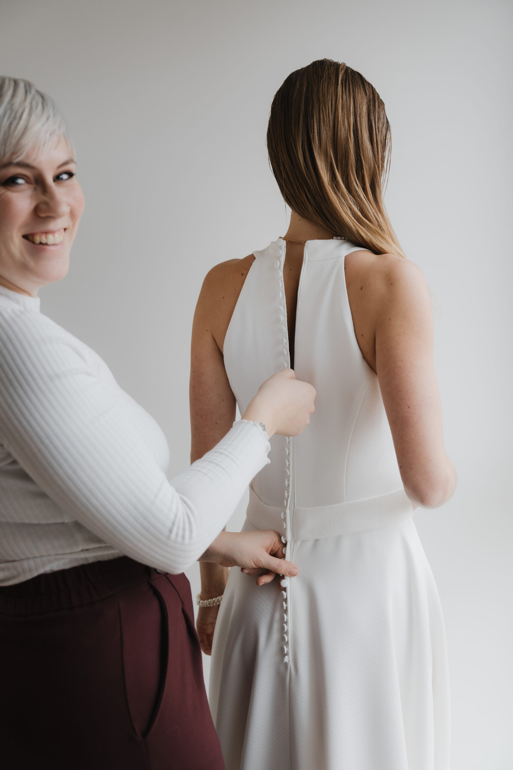 Hochzeitsplanerin hilft Braut beim Brautkleid anziehen am Hochzeitstag